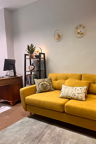 Cozy seating area featuring a gray armchair with colorful cushions and an orange accent chair, against a light green wall. Includes a small round table with a plant and decorative items, along with warm lighting. Ideal for interior design inspiration.