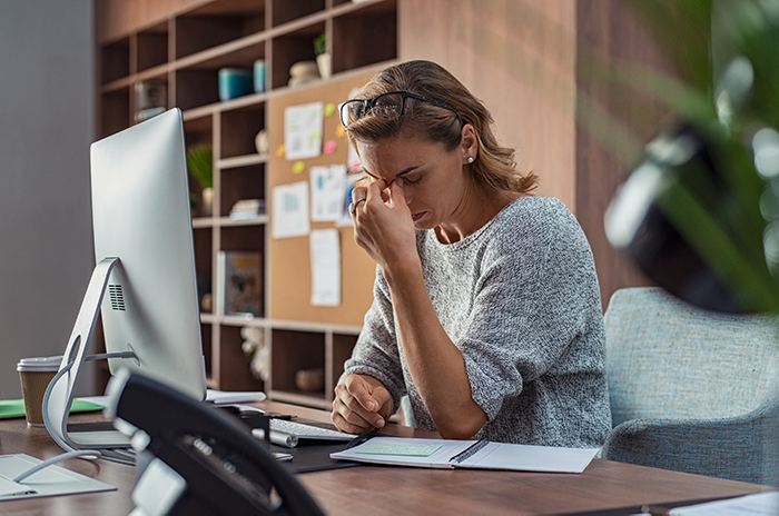 Stressed business woman pinching her brow while sitting at office desk